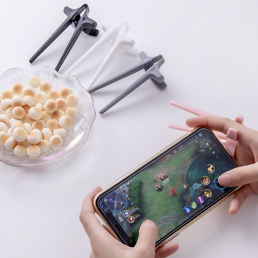 Person playing a game on a smartphone with a bowl of snacks and phone stands on a white surface
